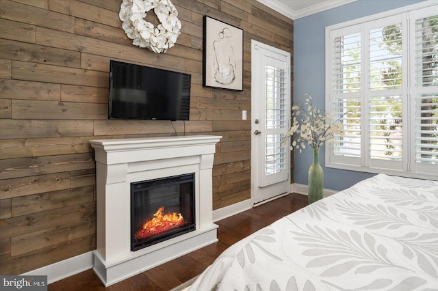 bedroom with crown molding, baseboards, dark wood finished floors, wood walls, and a glass covered fireplace