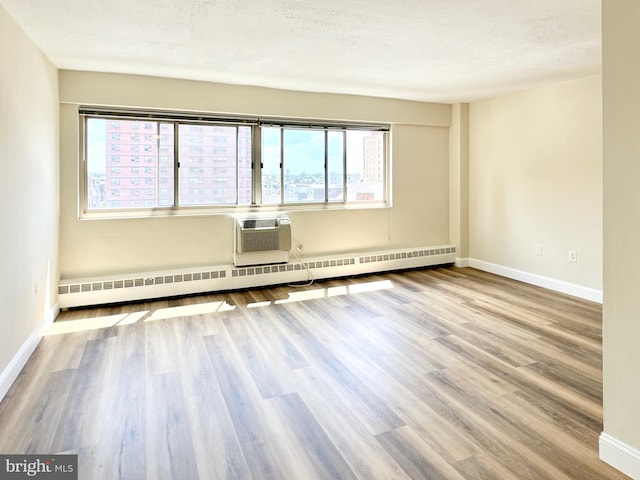 spare room featuring a baseboard heating unit, baseboards, wood finished floors, and an AC wall unit