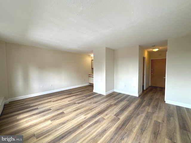 empty room featuring dark wood-style flooring, baseboards, and a textured ceiling