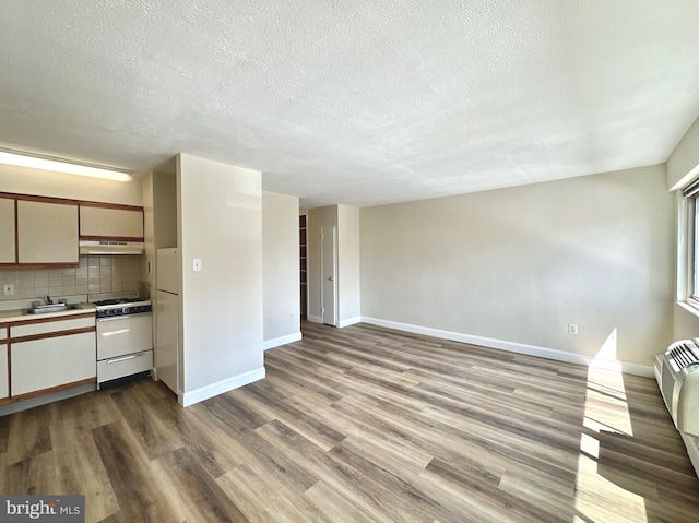 kitchen with white appliances, wood finished floors, under cabinet range hood, a textured ceiling, and baseboards
