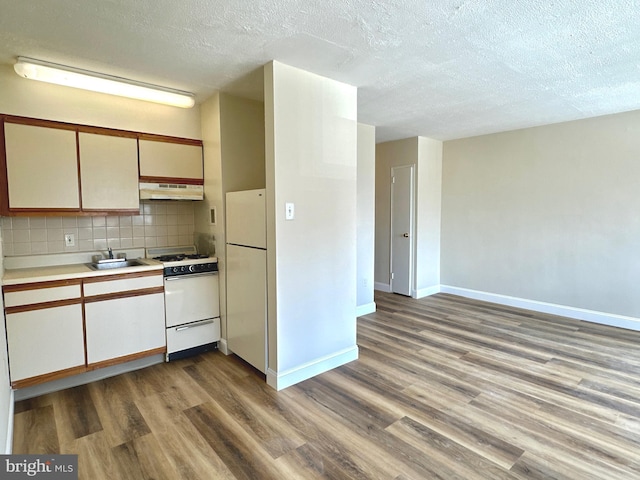 kitchen featuring white appliances, under cabinet range hood, a sink, a textured ceiling, and wood finished floors
