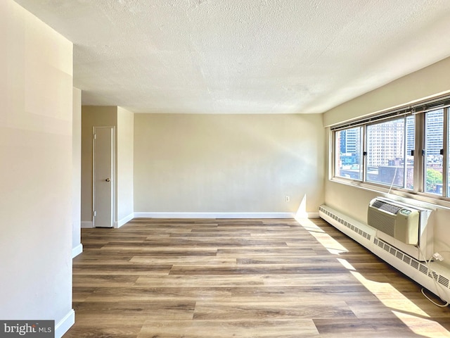 unfurnished room featuring wood finished floors, a textured ceiling, baseboard heating, baseboards, and a wall mounted AC