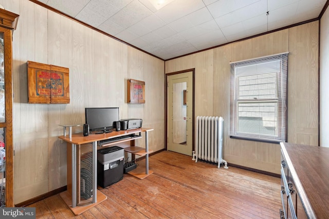 office space with crown molding, light wood finished floors, wood walls, and radiator