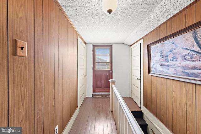 hall featuring vaulted ceiling, wood walls, an upstairs landing, and hardwood / wood-style flooring