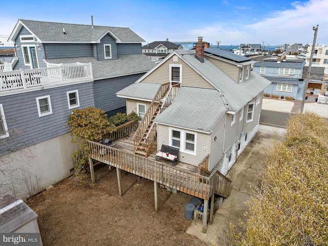 rear view of house with stairs, a deck, and roof with shingles