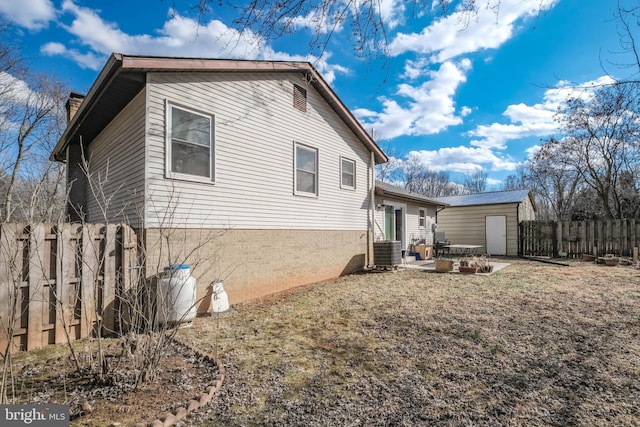 view of side of property featuring central AC unit, a fenced backyard, an outbuilding, a patio area, and brick siding