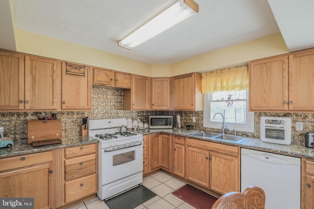 kitchen with tasteful backsplash, light tile patterned flooring, a sink, dark stone counters, and white appliances