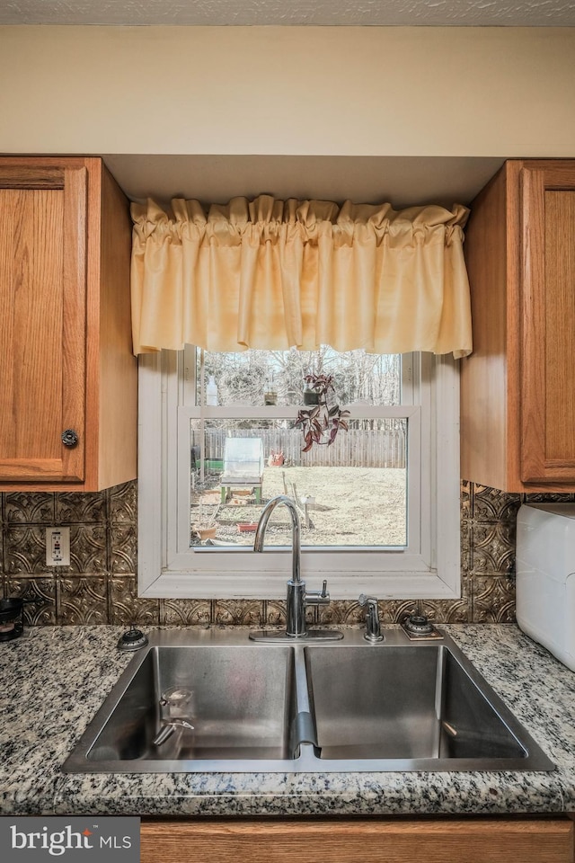 kitchen featuring tasteful backsplash, dark stone countertops, brown cabinets, and a sink