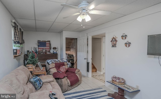 living room featuring a paneled ceiling, ceiling fan, stairs, and light tile patterned flooring