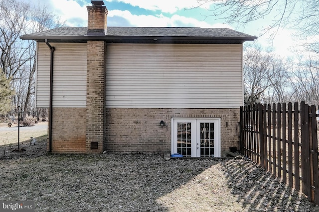 rear view of property with brick siding, a chimney, fence, and french doors