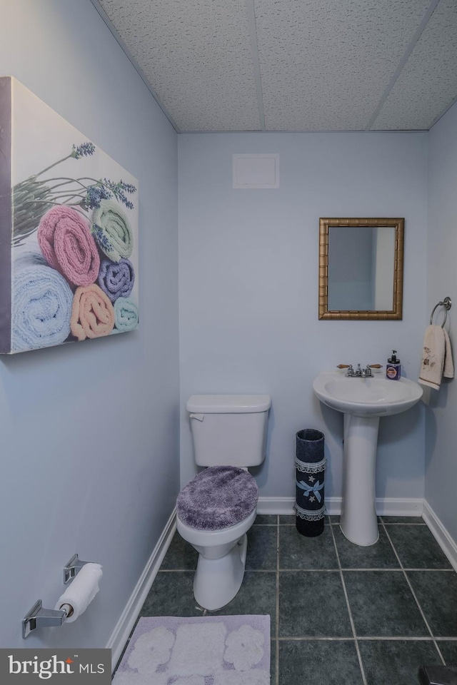 half bath with baseboards, a drop ceiling, toilet, and tile patterned floors