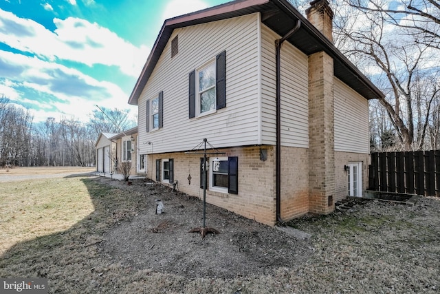 view of side of property with brick siding, fence, a chimney, and a lawn