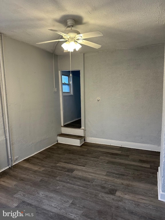 empty room with a textured ceiling, ceiling fan, dark wood-type flooring, and baseboards