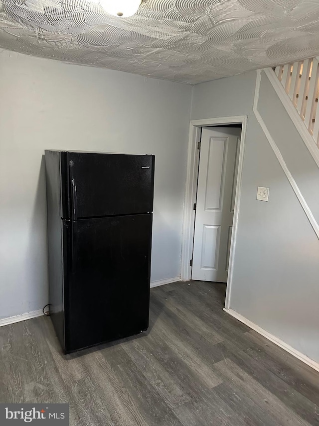 kitchen with dark wood-type flooring, freestanding refrigerator, and baseboards