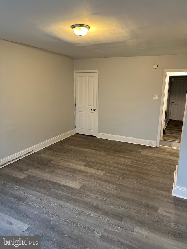 spare room featuring dark wood-style floors and baseboards