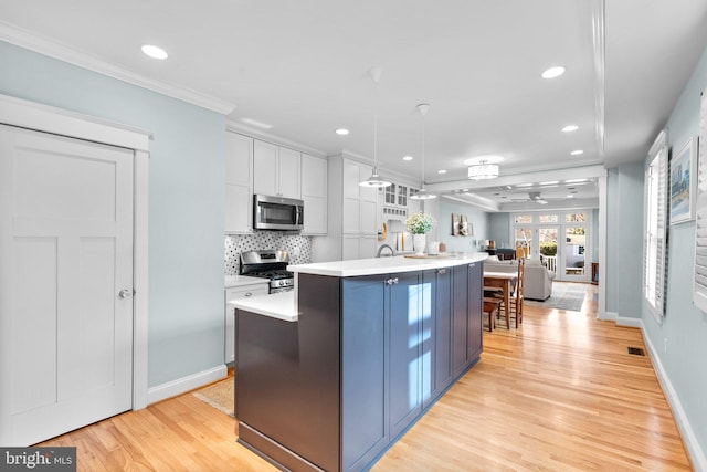 kitchen with stainless steel appliances, crown molding, light countertops, light wood-style floors, and backsplash