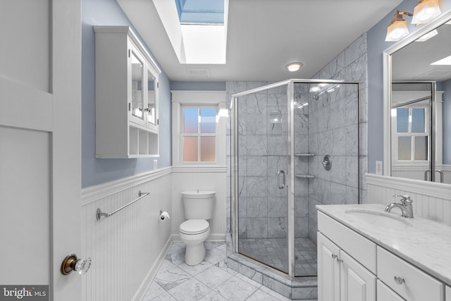 bathroom with a skylight, a stall shower, wainscoting, toilet, and marble finish floor