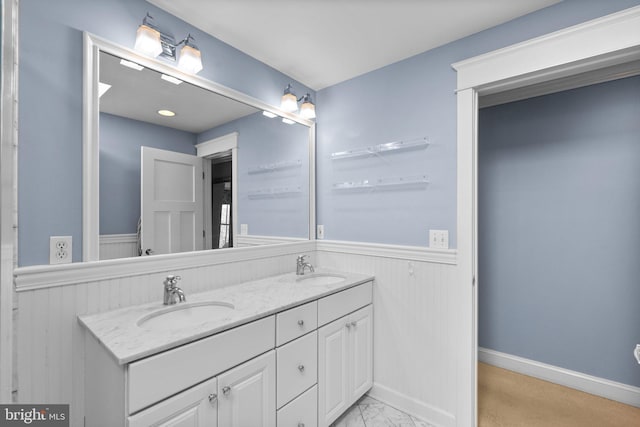 full bath with double vanity, a wainscoted wall, marble finish floor, and a sink