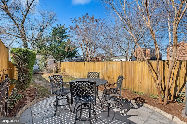 view of patio featuring outdoor dining space, a fenced backyard, and an outbuilding