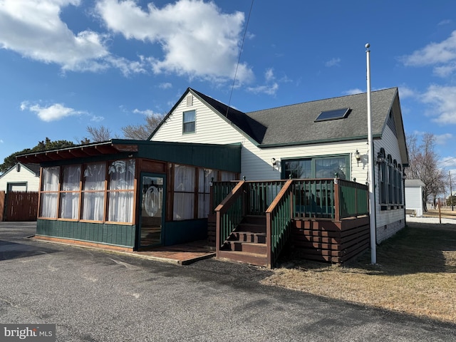 bungalow-style house with a sunroom, roof with shingles, and a wooden deck