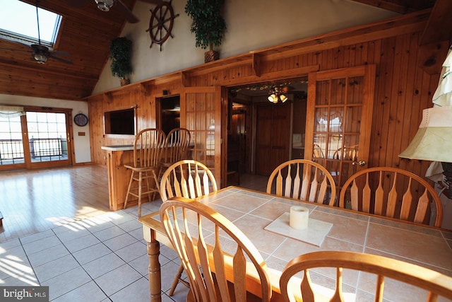 tiled dining area featuring high vaulted ceiling, a skylight, and wood walls