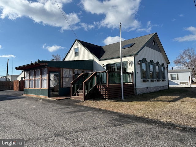 view of front facade with crawl space, a sunroom, a shingled roof, and a deck