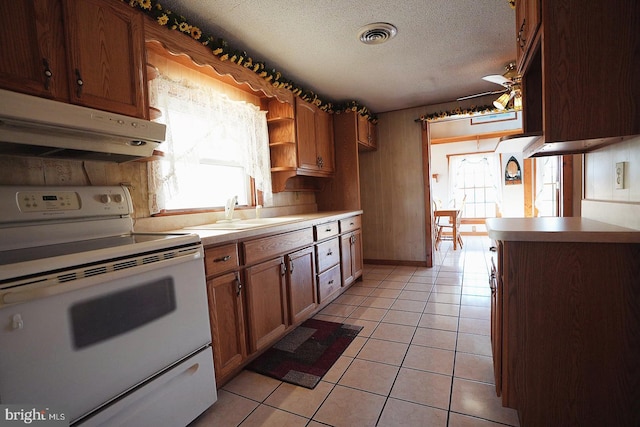 kitchen featuring light tile patterned flooring, under cabinet range hood, electric range, a sink, and visible vents