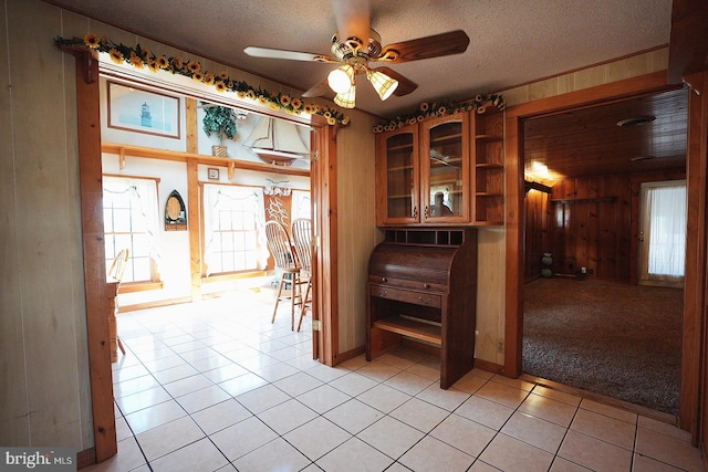 unfurnished dining area featuring wood walls, ceiling fan, a textured ceiling, and light tile patterned floors