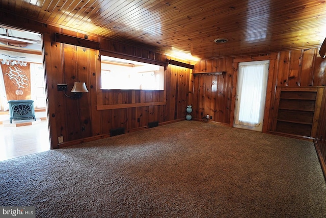 spare room featuring a wood stove, wood walls, wood ceiling, and carpet floors