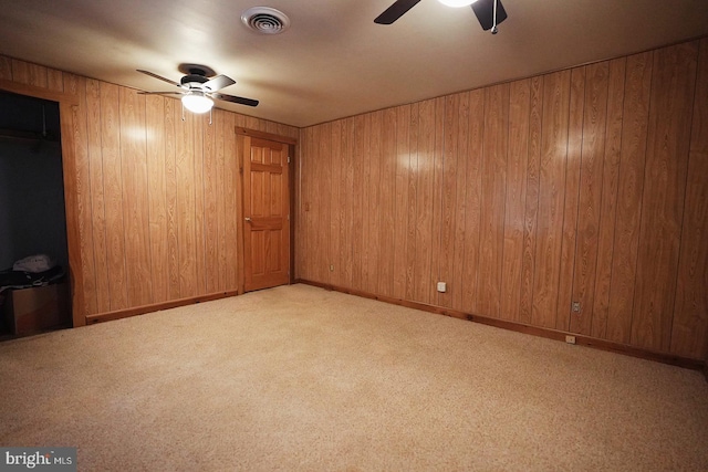 unfurnished room with ceiling fan, wooden walls, visible vents, and carpet flooring