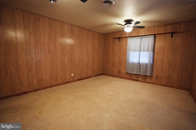 unfurnished room featuring visible vents, a ceiling fan, light carpet, wooden walls, and baseboards