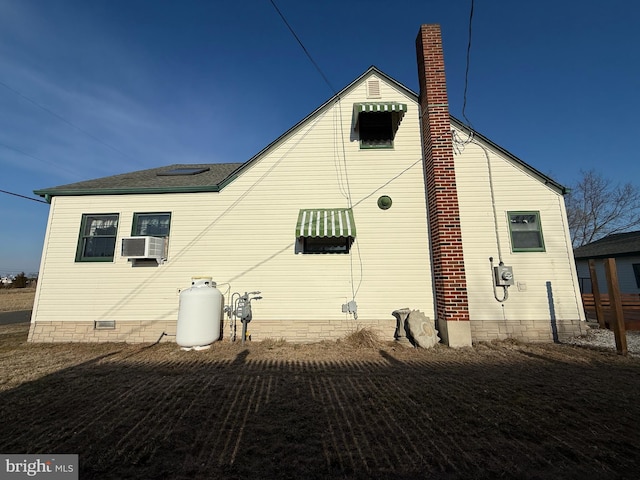 rear view of house with a shingled roof, cooling unit, crawl space, and a chimney