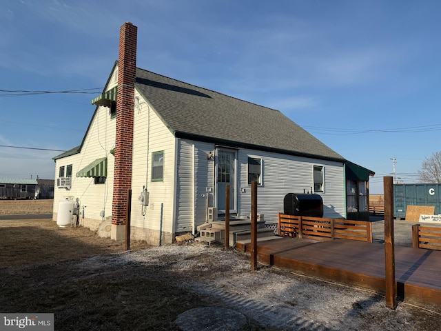 rear view of house featuring a shingled roof, a chimney, and a wooden deck