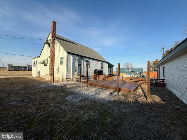 rear view of house with a shingled roof, a chimney, and a deck