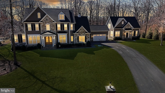 view of front of home with a garage, stone siding, a front lawn, and aphalt driveway