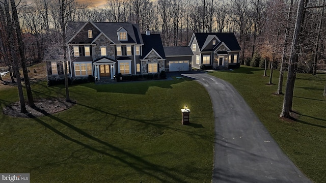 view of front facade featuring driveway, a garage, stone siding, a chimney, and a yard