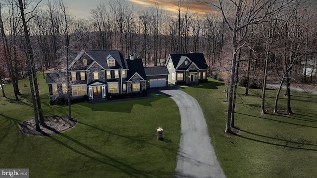 view of front facade with driveway, stone siding, a wooded view, and a lawn