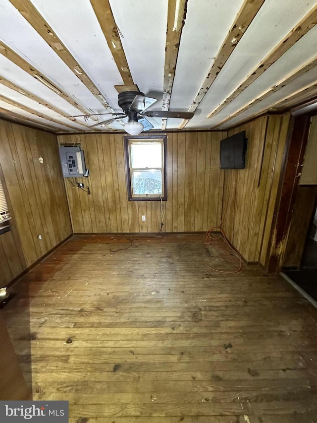 basement with dark wood-style floors, electric panel, a ceiling fan, and wooden walls