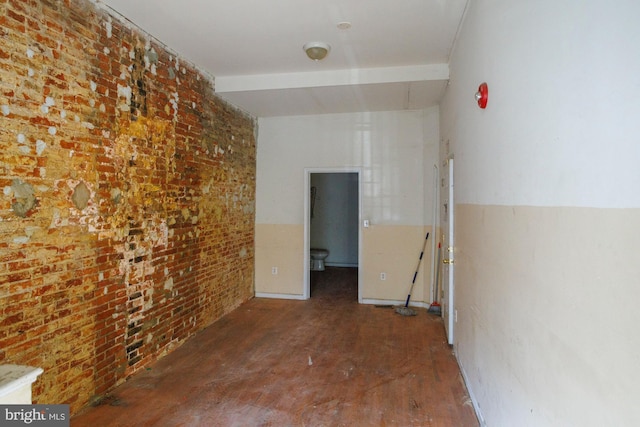 unfurnished room with brick wall and wood finished floors