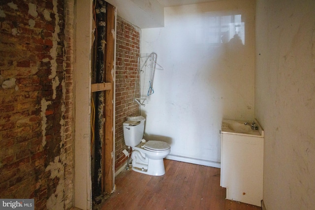 bathroom featuring toilet, brick wall, and wood finished floors