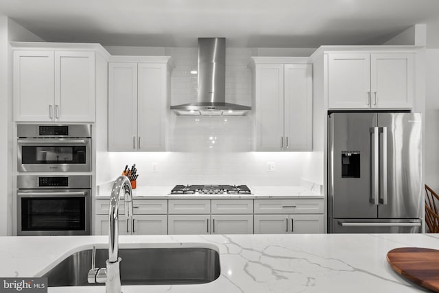 kitchen featuring a sink, stainless steel appliances, white cabinetry, wall chimney exhaust hood, and tasteful backsplash