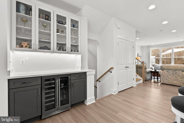 bar featuring light wood-type flooring, beverage cooler, backsplash, recessed lighting, and a bar