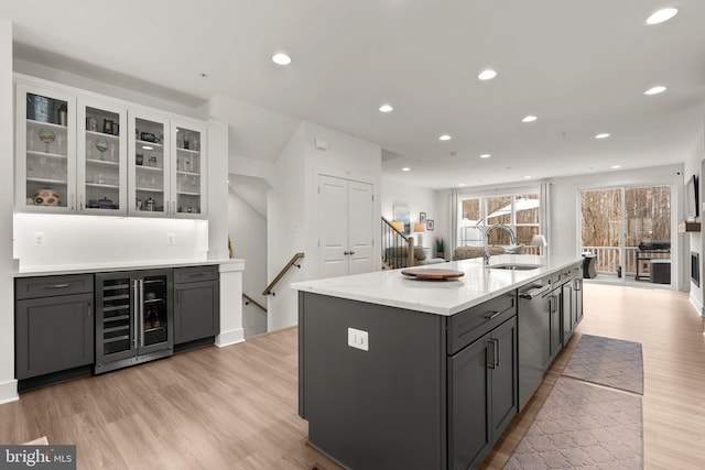 kitchen featuring a sink, beverage cooler, light wood-type flooring, recessed lighting, and a kitchen island with sink