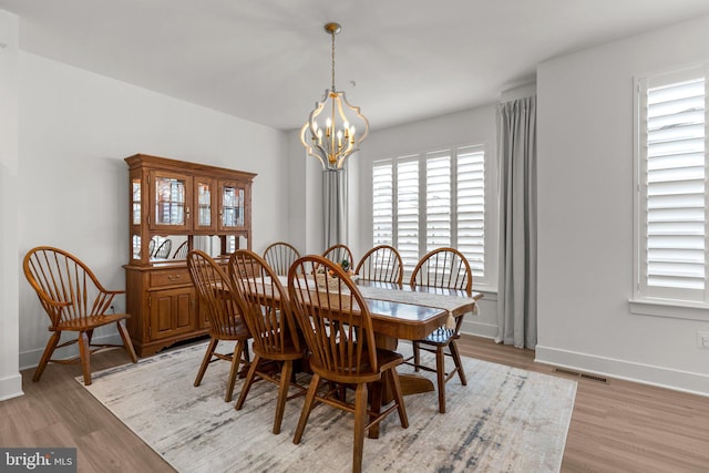 dining room featuring light wood finished floors, visible vents, baseboards, and an inviting chandelier