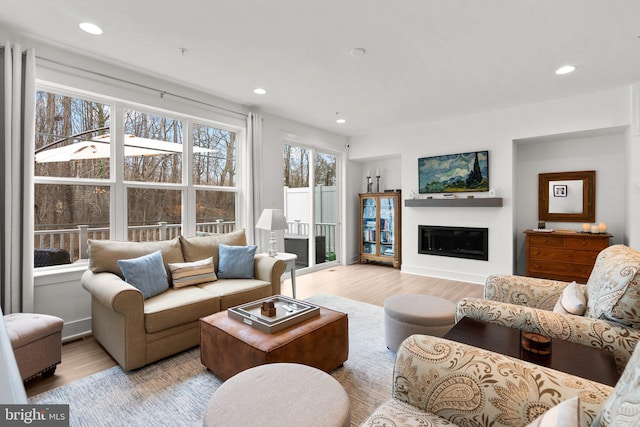 living area with a glass covered fireplace, recessed lighting, light wood-type flooring, and baseboards