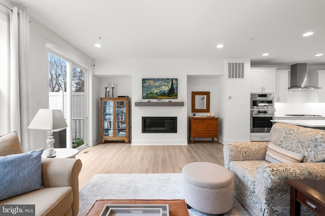 living room with visible vents, baseboards, recessed lighting, light wood-style flooring, and a glass covered fireplace