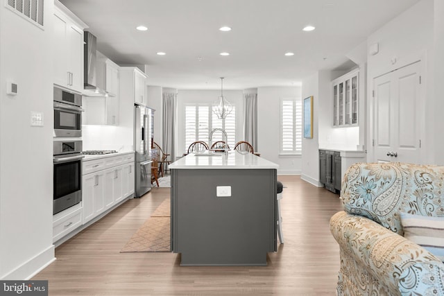 kitchen featuring visible vents, a kitchen island with sink, stainless steel appliances, white cabinets, and wall chimney exhaust hood