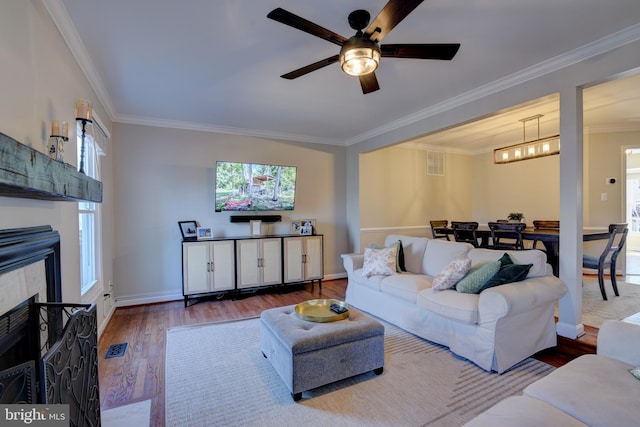 living room with crown molding, visible vents, a tiled fireplace, wood finished floors, and baseboards