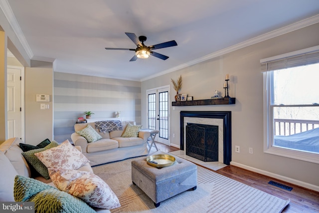 living area featuring a fireplace with flush hearth, wood finished floors, visible vents, baseboards, and crown molding