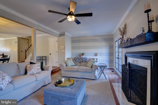 living area featuring a fireplace with flush hearth, ornamental molding, ceiling fan, wood finished floors, and stairs